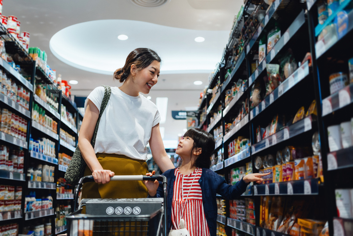 Young Asian mother shopping with her little daughter in supermarket joyfully. They are pushing a shopping cart, walking along the product aisle shopping for groceries and daily necessities. Shopping healthy food for family. Sustainable eating lifestyle